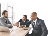 businessmen shaking hands around a conference table with computers and celll phones